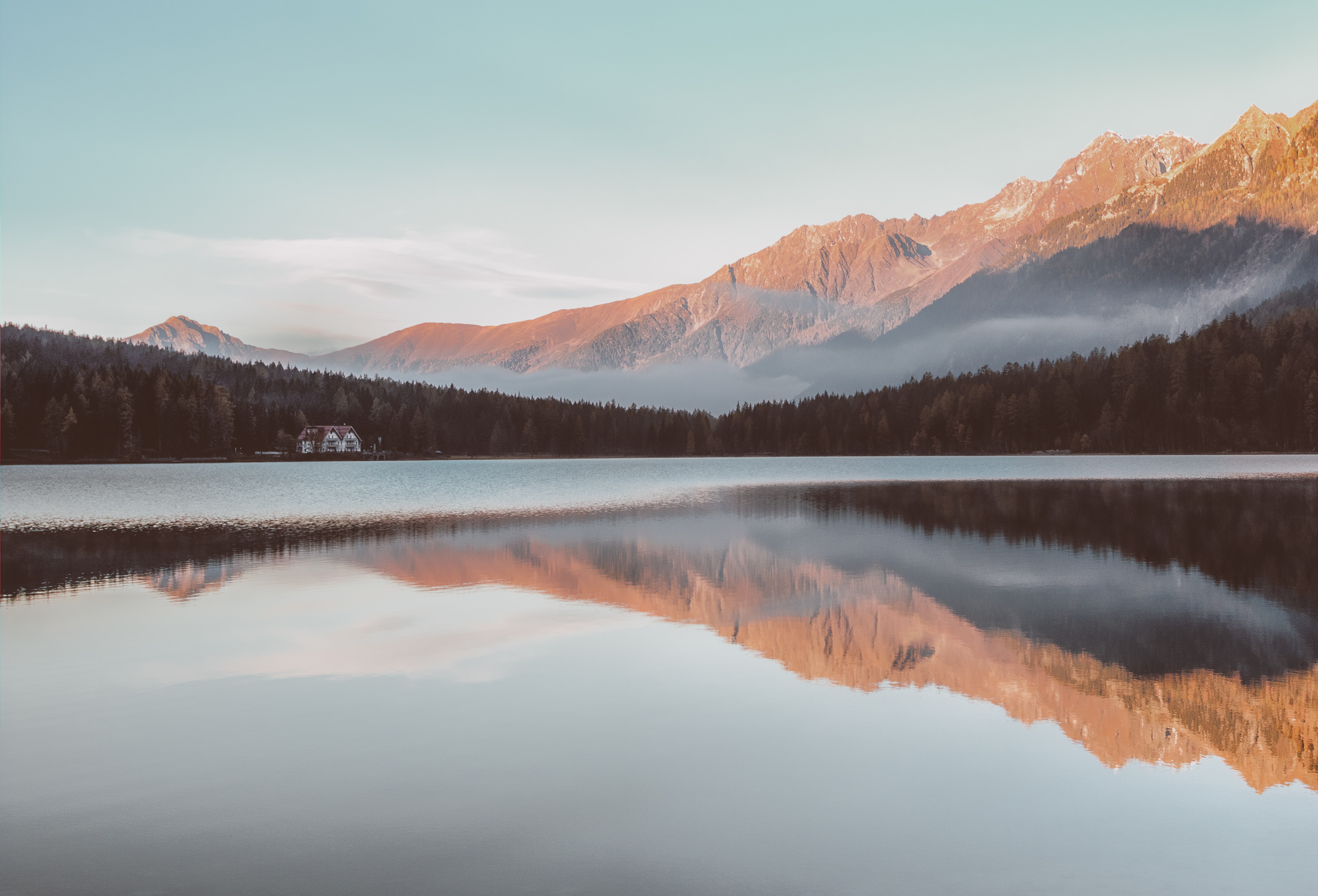 Alpine lake with cabin and mountain reflections at sunrise