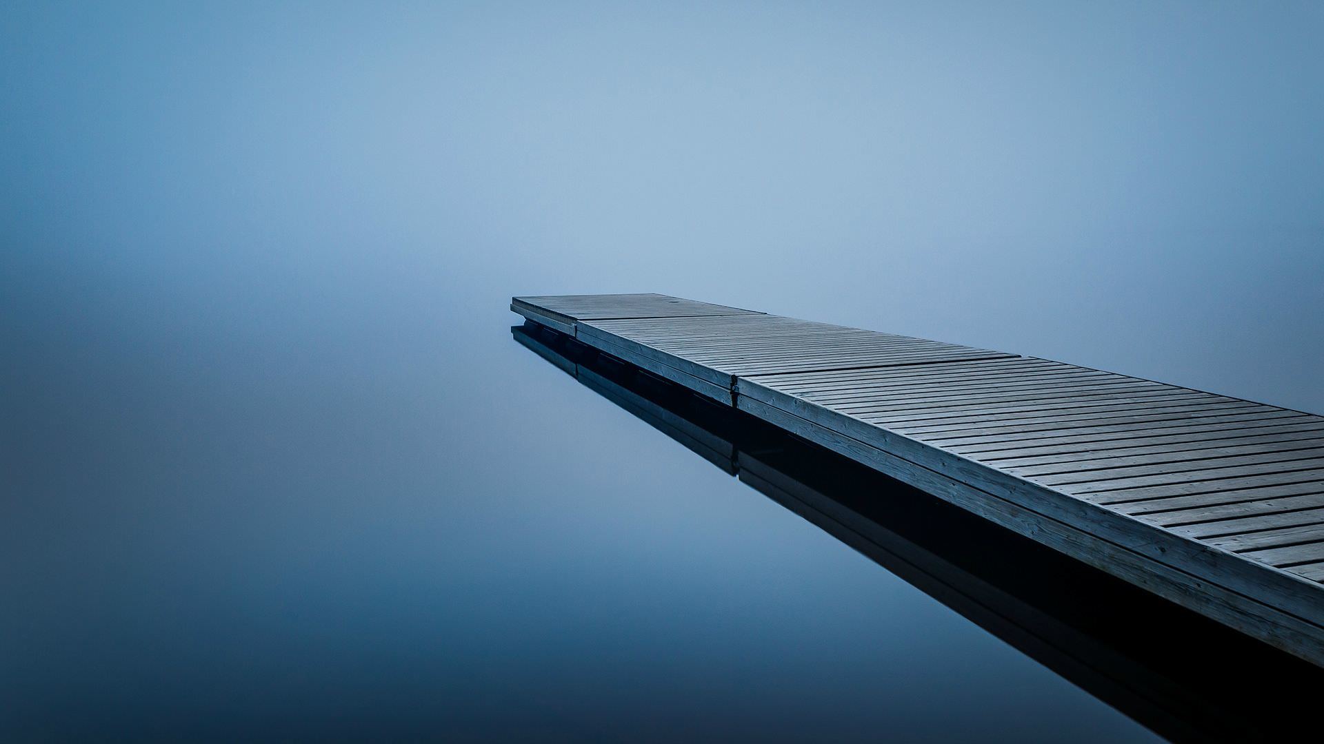 Wooden dock extending into perfectly still foggy water
