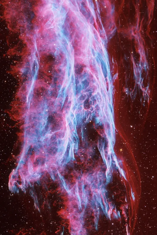 A vertical cascade of fine blue filaments in the Veil Nebula, edged in magenta and crimson