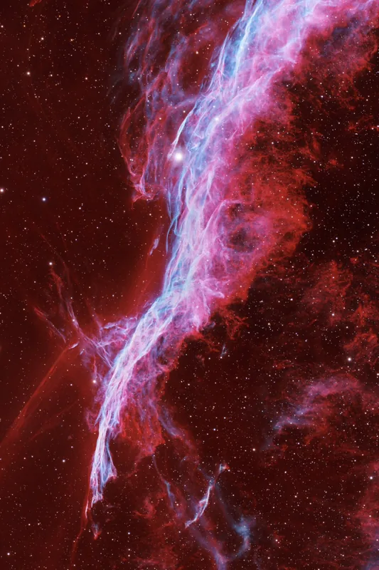 A curved shock ridge in the Veil Nebula sweeping from upper right to lower left, blue over faint red clouds